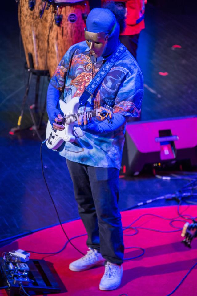 The/Theys guitarist in a blue mask and patterned shirt playing a white electric guitar