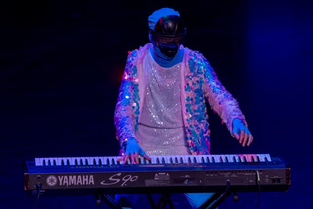 The/Theys keyboardist in a sequined jacket and mask playing a Yamaha S90